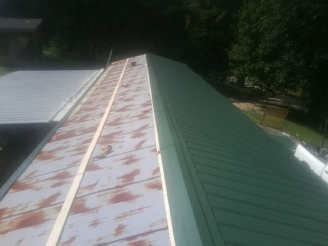 Old rusted panels beside newly installed green metal roofing — Wind Damage Roof Repair by Roofing Brothers in Hinton