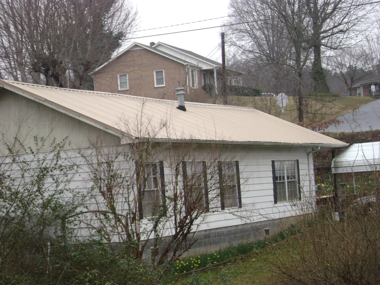 Tan metal roof on a white sided house set into a hillside — Commercial Roofing by Roofing Brothers in Hinton